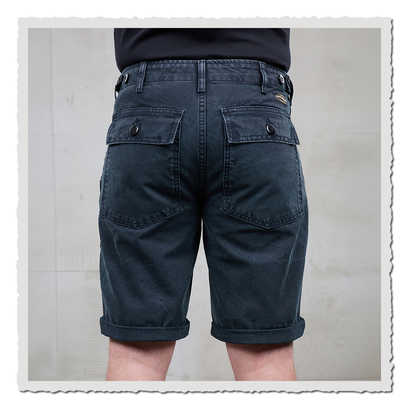 Dunkle Shorts von hinten getragen, vor hellem Hintergrund mit neutraler Wandfläche.